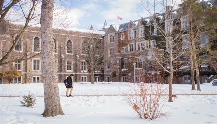 A person walks in front of a large stone building at McMaster during the winter time